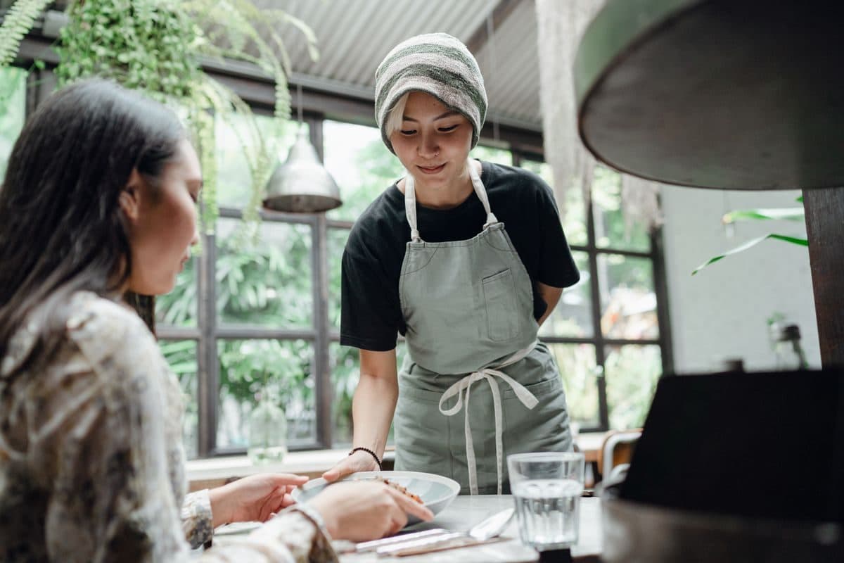 A server in an apron setting a plate down for a guest in a bright restaurant